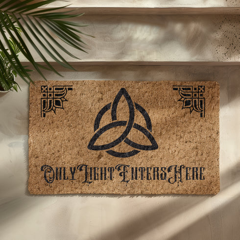 Coir doormat featuring large triple moon and triquetra symbol in center, surrounded by celestial designs including stars and moon phases, all in dark brown on natural tan background.